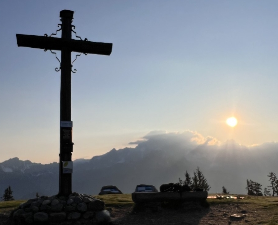 Das Gipfelkreuz vom Rossbrand wird von der aufgehenden Sonne angeleuchtet.